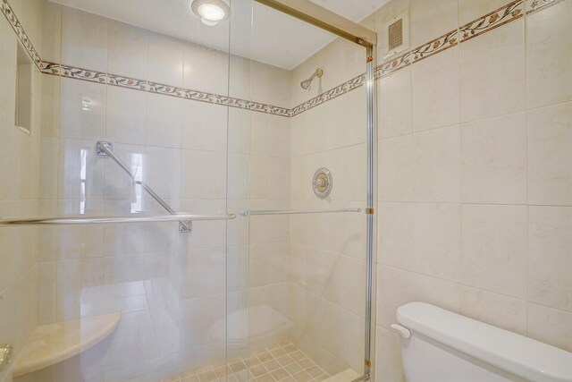 bathroom with tile walls, toilet, and an enclosed shower