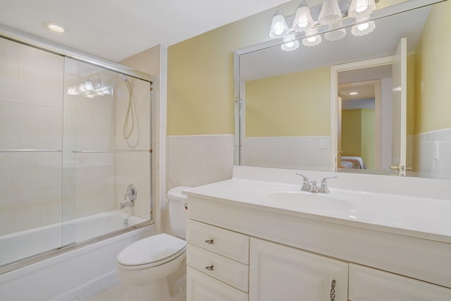 full bathroom featuring shower / bath combination with glass door, vanity, toilet, and tile walls