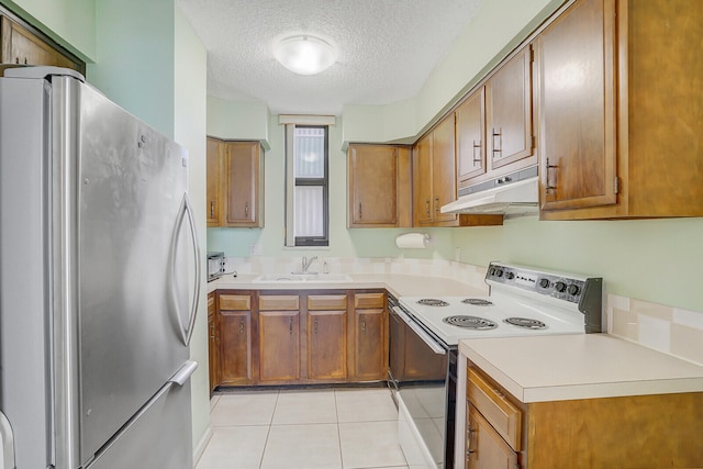 kitchen featuring light tile patterned floors, white range with electric cooktop, stainless steel refrigerator, sink, and a textured ceiling