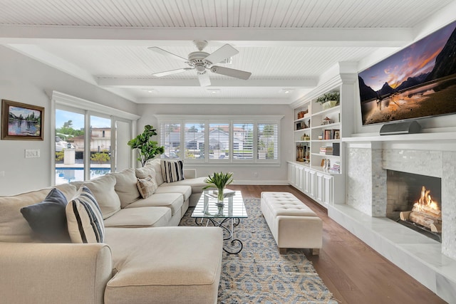 living room with wood-type flooring, a high end fireplace, ceiling fan, and beamed ceiling