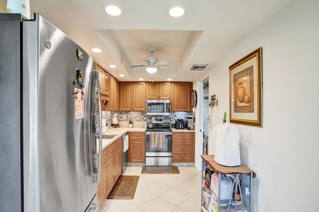 kitchen with backsplash, a raised ceiling, ceiling fan, light tile patterned floors, and appliances with stainless steel finishes