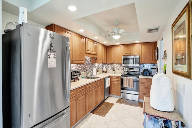 kitchen with backsplash, stainless steel appliances, a tray ceiling, sink, and light tile patterned floors