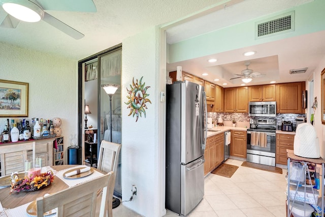 kitchen with backsplash, a raised ceiling, light tile patterned floors, a textured ceiling, and stainless steel appliances