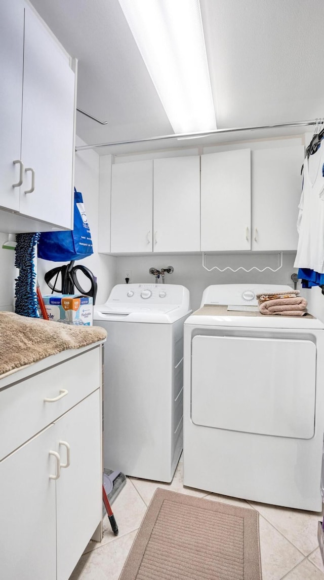 laundry area with washing machine and clothes dryer, light tile patterned floors, and cabinets