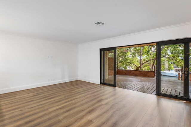 empty room featuring baseboards, wood finished floors, visible vents, and crown molding