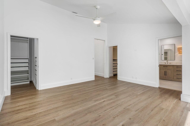 unfurnished bedroom with light wood finished floors, a spacious closet, a sink, high vaulted ceiling, and baseboards