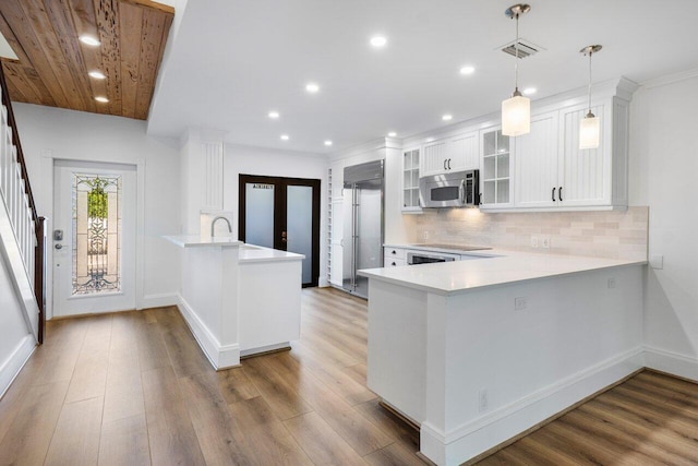 kitchen featuring a peninsula, wood finished floors, white cabinets, light countertops, and stainless steel microwave