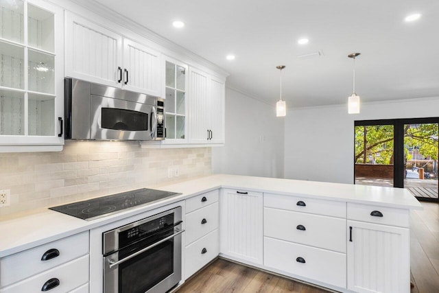 kitchen featuring appliances with stainless steel finishes, ornamental molding, wood finished floors, a peninsula, and light countertops