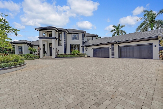 view of front of property with decorative driveway, an attached garage, and stucco siding