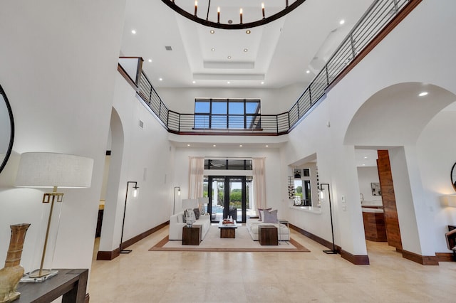 foyer entrance with a high ceiling, a notable chandelier, a tray ceiling, and french doors