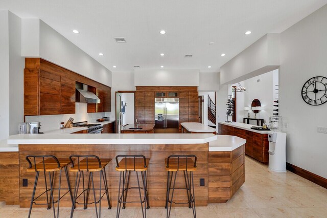 kitchen with a breakfast bar, kitchen peninsula, wall chimney exhaust hood, and premium appliances