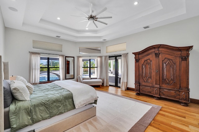 bedroom with french doors, light wood-type flooring, a raised ceiling, access to outside, and ceiling fan