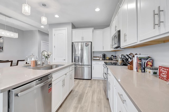 kitchen featuring light hardwood / wood-style flooring, decorative light fixtures, appliances with stainless steel finishes, white cabinetry, and sink