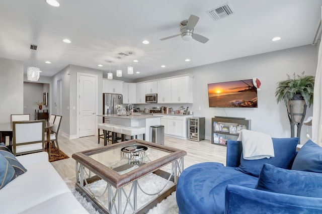 living room featuring light wood-type flooring, ceiling fan, wine cooler, and sink