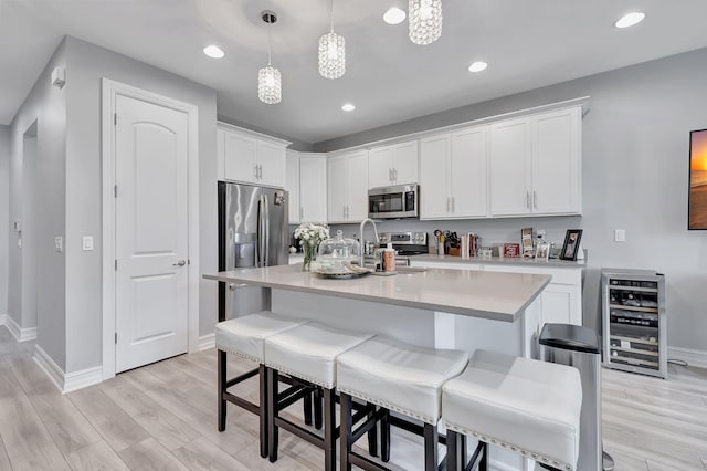 kitchen featuring stainless steel appliances, an island with sink, white cabinetry, and light hardwood / wood-style flooring