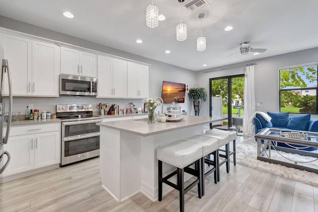 kitchen featuring a center island with sink, ceiling fan, appliances with stainless steel finishes, and white cabinetry