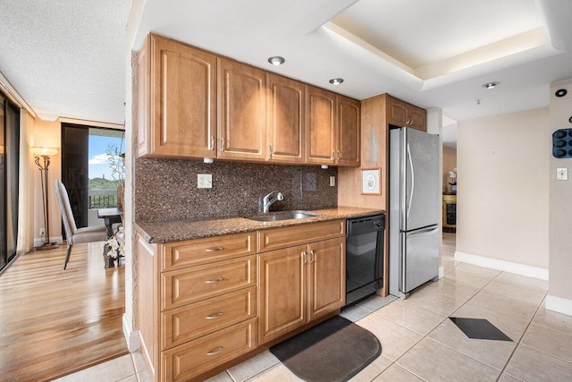 kitchen featuring dishwasher, dark stone countertops, sink, stainless steel refrigerator, and light tile patterned flooring