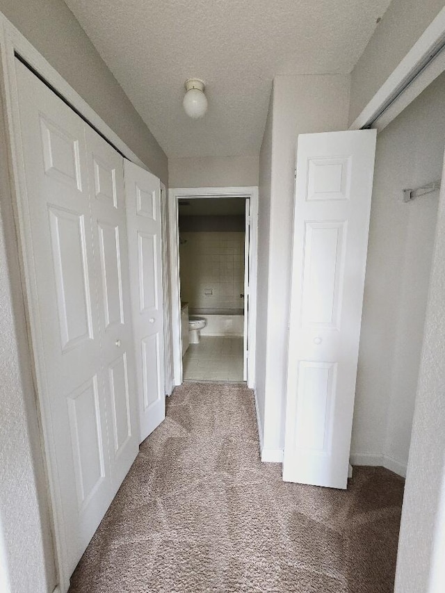 corridor featuring a textured ceiling, carpet, and baseboards