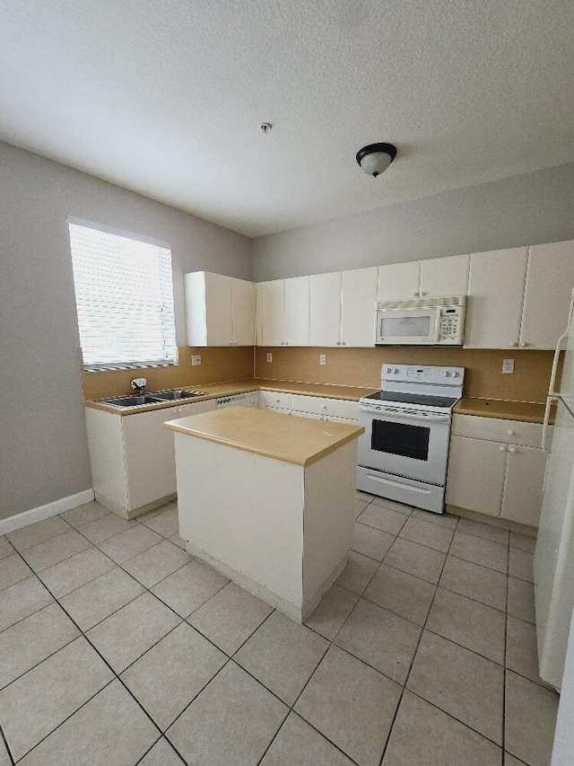 kitchen featuring light tile patterned flooring, sink, white appliances, a kitchen island, and white cabinets