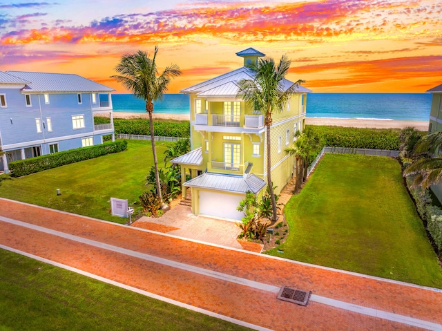 view of front of home with a garage, a beach view, a yard, a water view, and a balcony