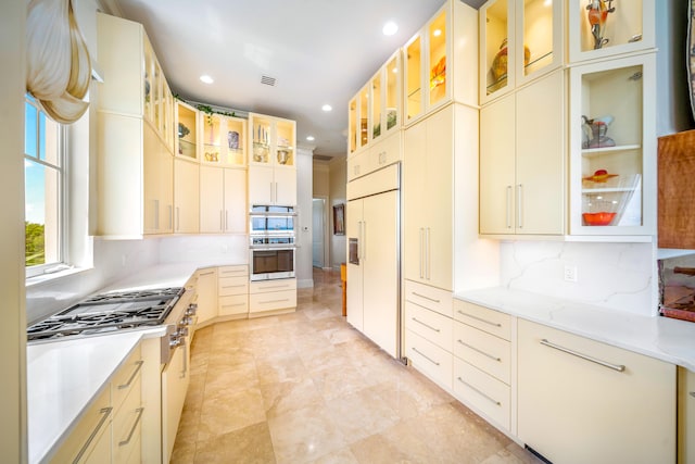 kitchen with cream cabinets, high quality appliances, light stone counters, and backsplash