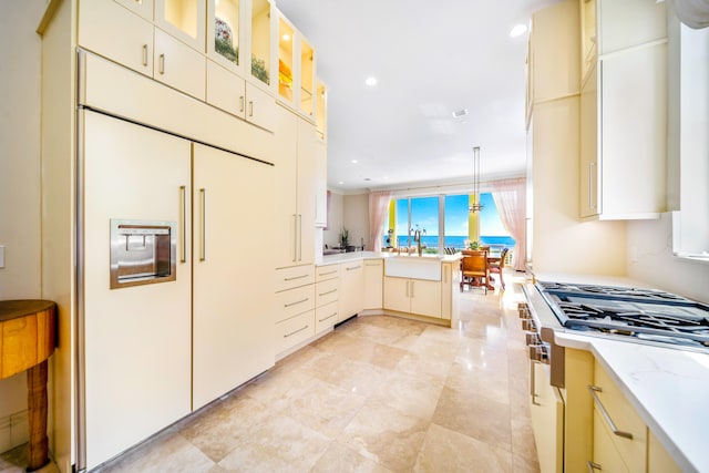 kitchen featuring paneled built in fridge, pendant lighting, stainless steel gas stovetop, kitchen peninsula, and cream cabinetry