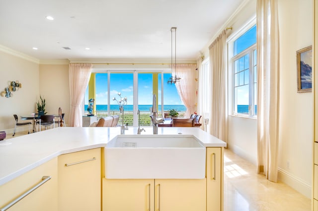 kitchen with hanging light fixtures, ornamental molding, a water view, and sink