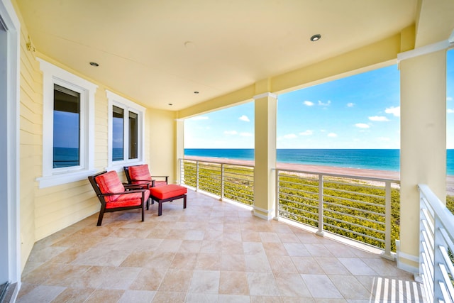 view of patio with a view of the beach, a water view, and a balcony