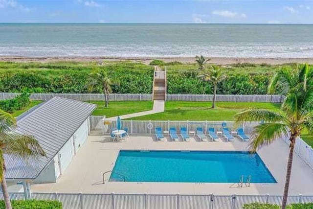 view of pool with a patio area, a water view, a view of the beach, and a yard