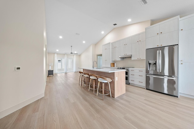 kitchen with stainless steel appliances, an island with sink, vaulted ceiling, a kitchen bar, and white cabinets