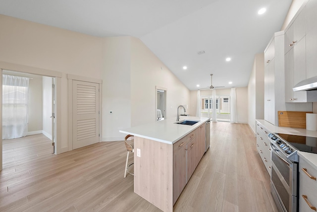 kitchen with light wood-type flooring, stainless steel appliances, ceiling fan, a kitchen island with sink, and sink