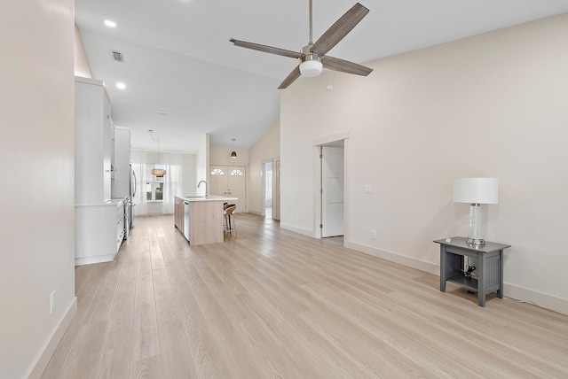 unfurnished living room with ceiling fan, sink, high vaulted ceiling, and light wood-type flooring