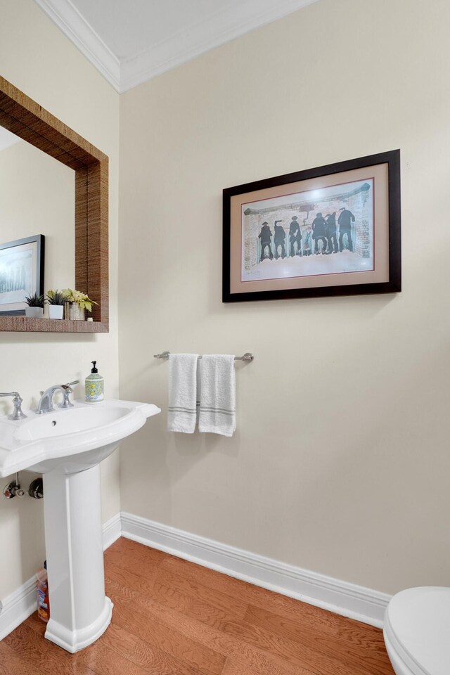 bathroom featuring baseboards, toilet, wood finished floors, crown molding, and a sink