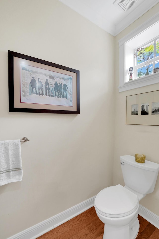 half bath with toilet, baseboards, visible vents, and wood finished floors