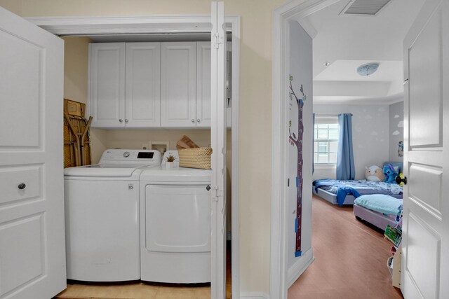 laundry room featuring washer and dryer, cabinet space, visible vents, and light wood finished floors