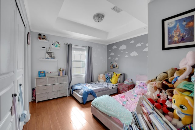 bedroom featuring hardwood / wood-style flooring, visible vents, a raised ceiling, and wallpapered walls