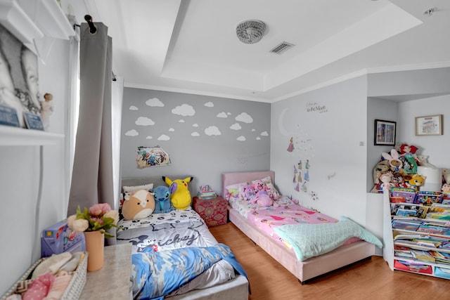 bedroom with visible vents, a tray ceiling, wood finished floors, and ornamental molding