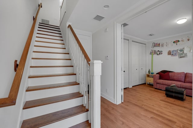 stairs with visible vents, crown molding, and wood finished floors