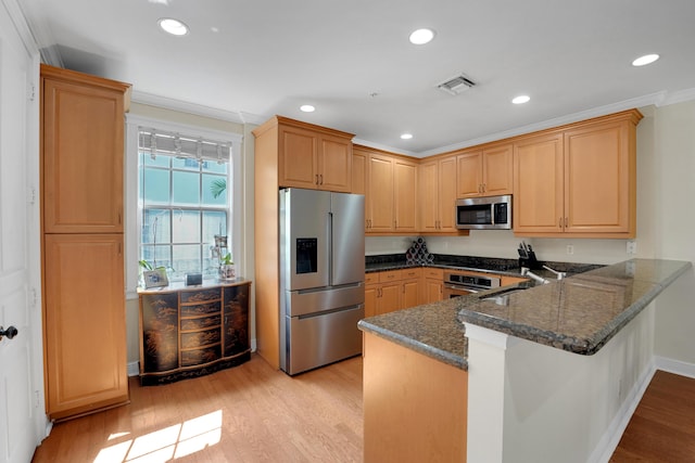 kitchen featuring a peninsula, appliances with stainless steel finishes, dark stone countertops, and light wood-style flooring