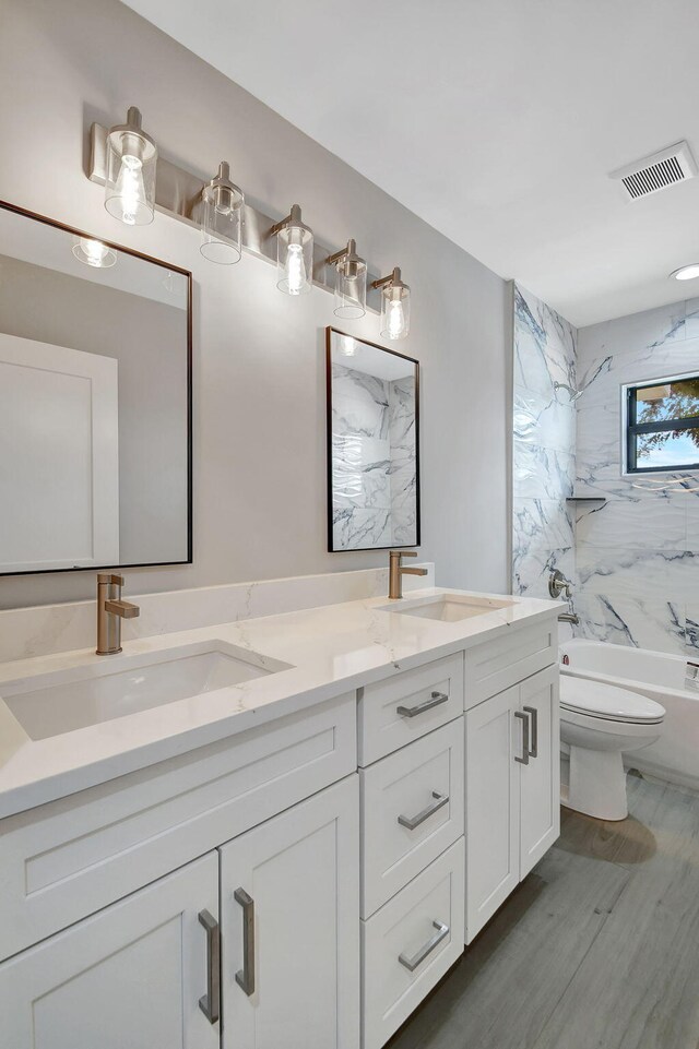 full bathroom featuring hardwood / wood-style floors, tiled shower / bath combo, toilet, and vanity