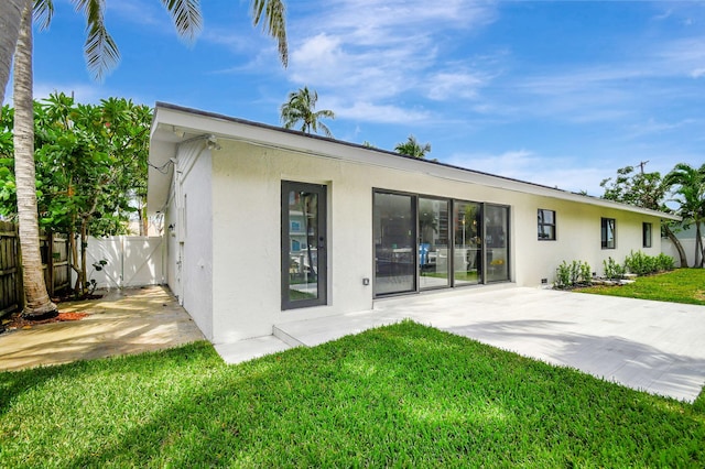 rear view of property with a patio area, fence, a lawn, and stucco siding