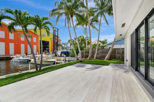 wooden deck with a water view, a dock, and fence