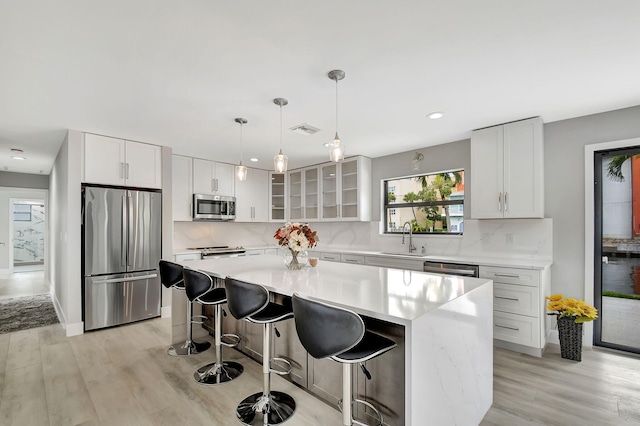 kitchen with white cabinets, light wood-type flooring, appliances with stainless steel finishes, and a kitchen island