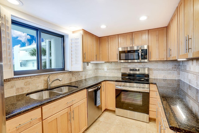 kitchen featuring dark stone countertops, stainless steel appliances, sink, decorative backsplash, and light brown cabinets