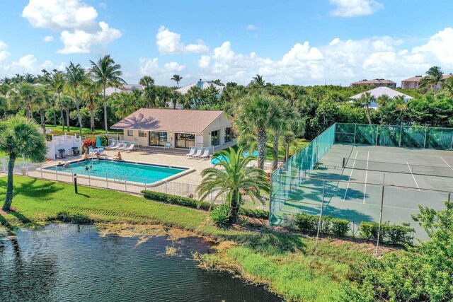 view of swimming pool with a patio area, tennis court, a lawn, and a water view