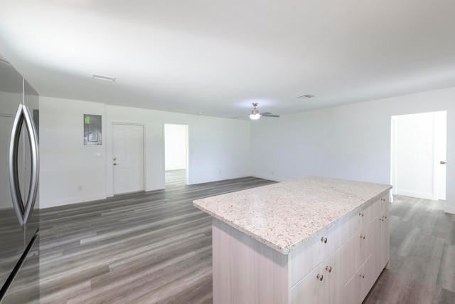 kitchen featuring hardwood / wood-style flooring, a center island, light stone countertops, stainless steel fridge, and ceiling fan