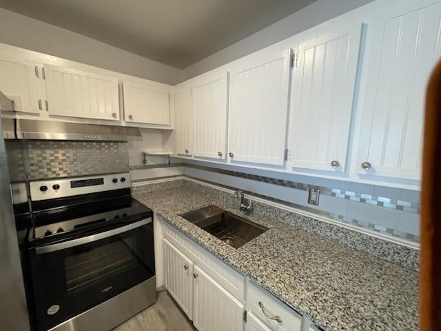 kitchen featuring stainless steel range with electric cooktop, light stone counters, white cabinets, and sink