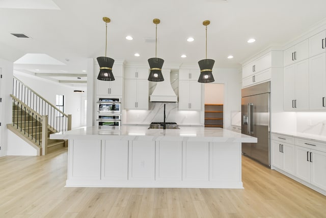 kitchen with custom exhaust hood, a large island, appliances with stainless steel finishes, light wood-type flooring, and pendant lighting