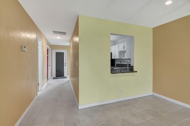 hall with a textured ceiling, light tile patterned floors, and sink