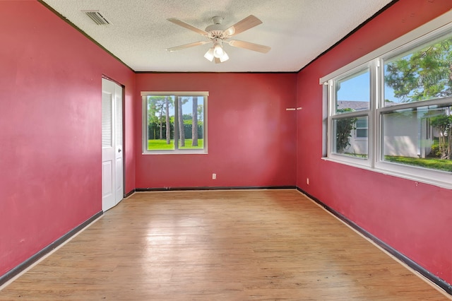 empty room with a textured ceiling, light hardwood / wood-style floors, a healthy amount of sunlight, and ceiling fan